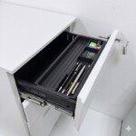 Close-up of the top drawer of an iSimply white steel pedestal, showing the integrated recessed handle and a black removable stationery tray for office supplies.