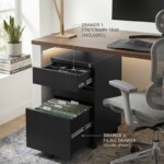 Lifestyle image of an iSimply black steel pedestal with open drawers: top drawer showing an included stationery tray and bottom drawer containing green suspended filing folders under a modern wooden desk.