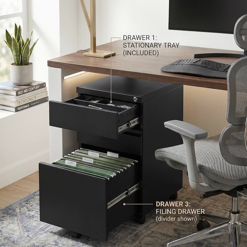 Lifestyle image of an iSimply black steel pedestal with open drawers: top drawer showing an included stationery tray and bottom drawer containing green suspended filing folders under a modern wooden desk.