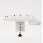 White clamp-on desktop power module against a clean light grey background, featuring three UK power sockets, a USB-A port with an orange interior, a USB-C port, a power switch, and a coiled white cable.