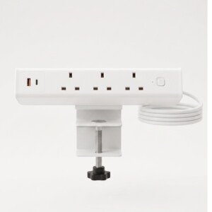 White clamp-on desktop power module against a clean light grey background, featuring three UK power sockets, a USB-A port with an orange interior, a USB-C port, a power switch, and a coiled white cable.
