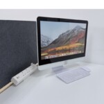 White clamp-on desktop power module in use on a white desk with a acostic panel in a office environment, illustrating a clean, organised workspace.