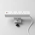 A clean, professional studio shot of the white Desktop Power Module from a top-down perspective. The image shows the integrated C-clamp with a black star knob, the smooth top surface of the module, and the power cord extending to the right against a neutral light grey background.