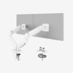A white FlexiSpot F5D-W dual monitor arm attached to a desk, holding two computer screens. The image highlights the two installation methods: a secure C-clamp attached to the edge of the desk, and a diagram showing the alternative grommet hole mounting option through the desk surface.