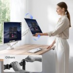 A woman standing at a desk effortlessly adjusting the angle and height of one of her two computer screens, which are mounted on a white FlexiSpot F5D-W dual monitor arm.