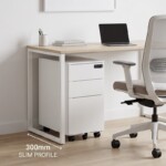 Wide-angle view of a modern office featuring a white iSimply Narrow Pedestal with a 300mm slim profile, perfectly fitted under a wooden desk and chair, demonstrating its under-desk space-saving design.